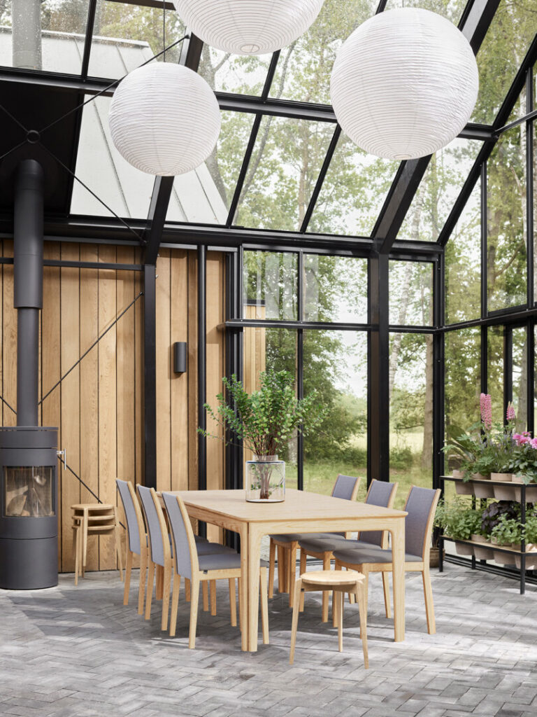 Photorealistic 3D visualization of a winter garden with glass walls, featuring a dining table and chairs in a light-filled interior, created by Nordic Render.